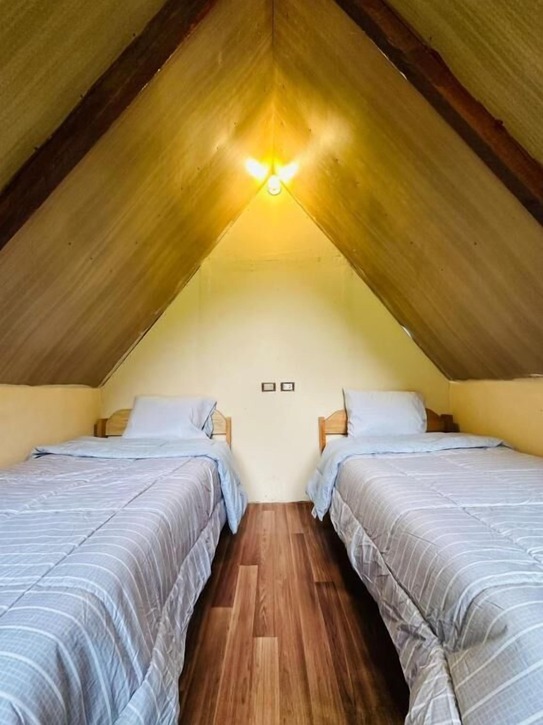 Un pequeño dormitorio en el ático con dos camas individuales, suelo de madera y techo inclinado con vigas a la vista.