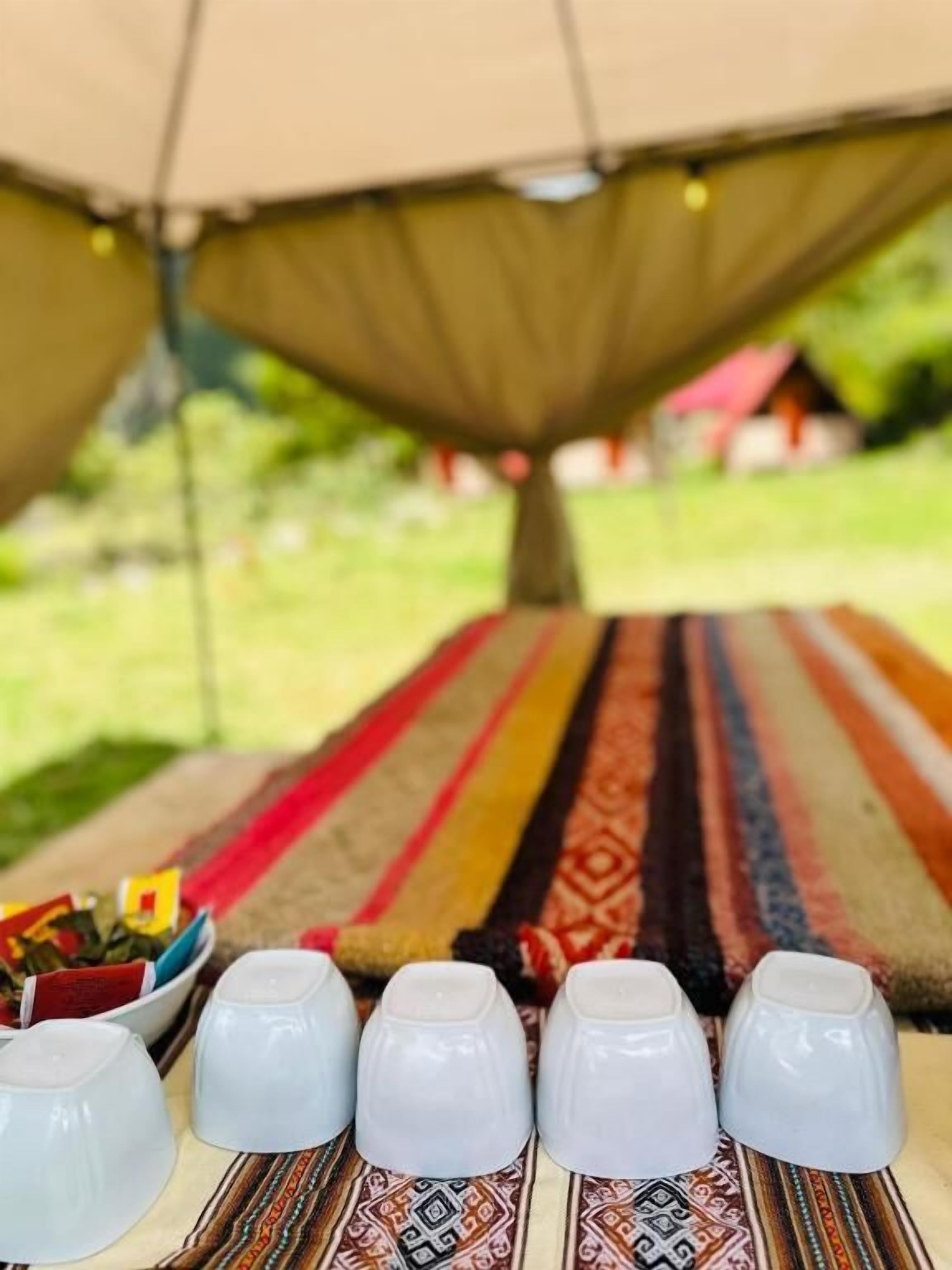 A dining area with a long table covered by a striped tablecloth, white cups, and a bowl of condiments.