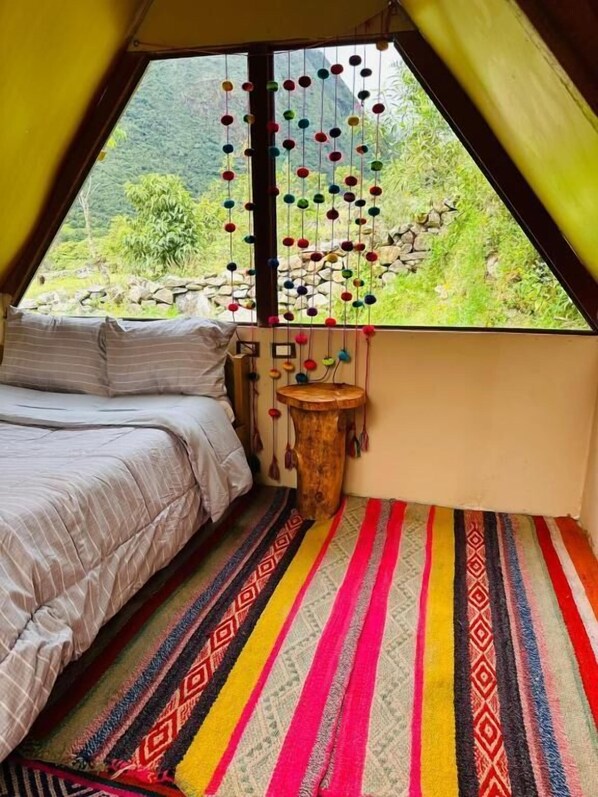 Una habitación acogedora con una cama, alfombra a rayas colorida y una decoración colgante, con vistas al exterior.