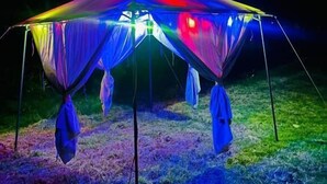 A large, open-sided tent with a flat top and multiple entry points, set up on a grassy area at night. - Salakantay glamp (Santa Teresa)