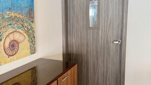 Una habitación con un armario de madera, una puerta gris con manija y un cuadro en la pared.