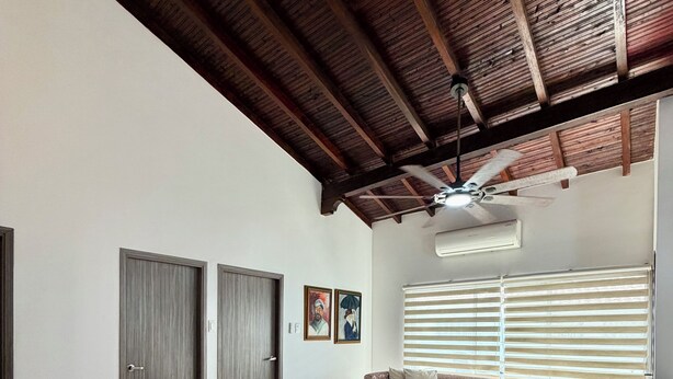 Amplia sala de estar con techo alto, ventilador de techo y un gran ventanal con persianas.