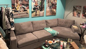 Un saló amb un sofà seccional gris, una taula de centre de vidre amb aperitius, i obra d'art a la paret que representa músics.