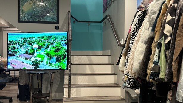 Un interior modern amb una escala, un televisor de pantalla plana que mostra un paisatge urbà i una estant de roba amb diverses peces.