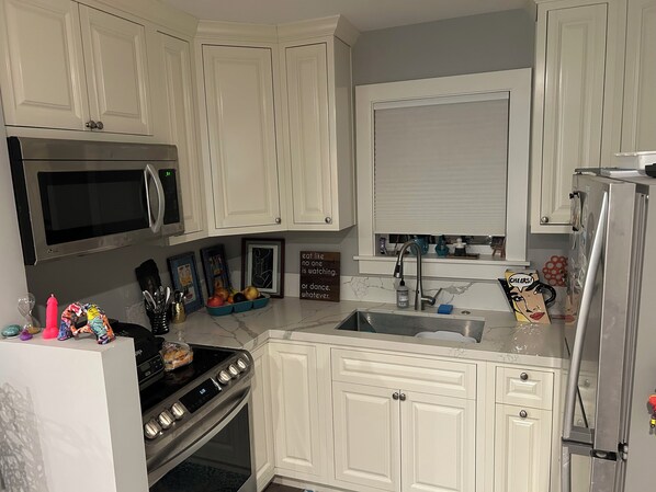 A kitchen with white cabinets, a microwave, a stove, and a refrigerator. There are framed pictures on the wall and a sign with a message.