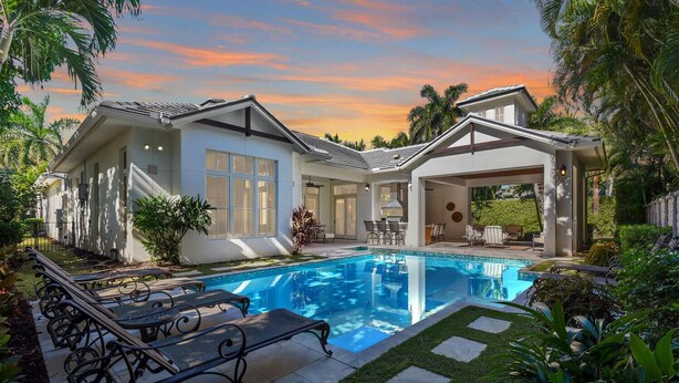 A modern house with a swimming pool, surrounded by lush greenery and palm trees. - Elevated Coastal Living | Luxury 4BR Home + Den | Designed for the Perfect Getaway (Naples)