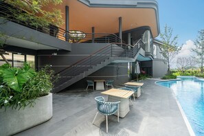 Ein moderner Außenpoolbereich mit einer Treppe zu einer erhöhten Ebene, umgeben von Pflanzkübeln und Gartenmöbeln.