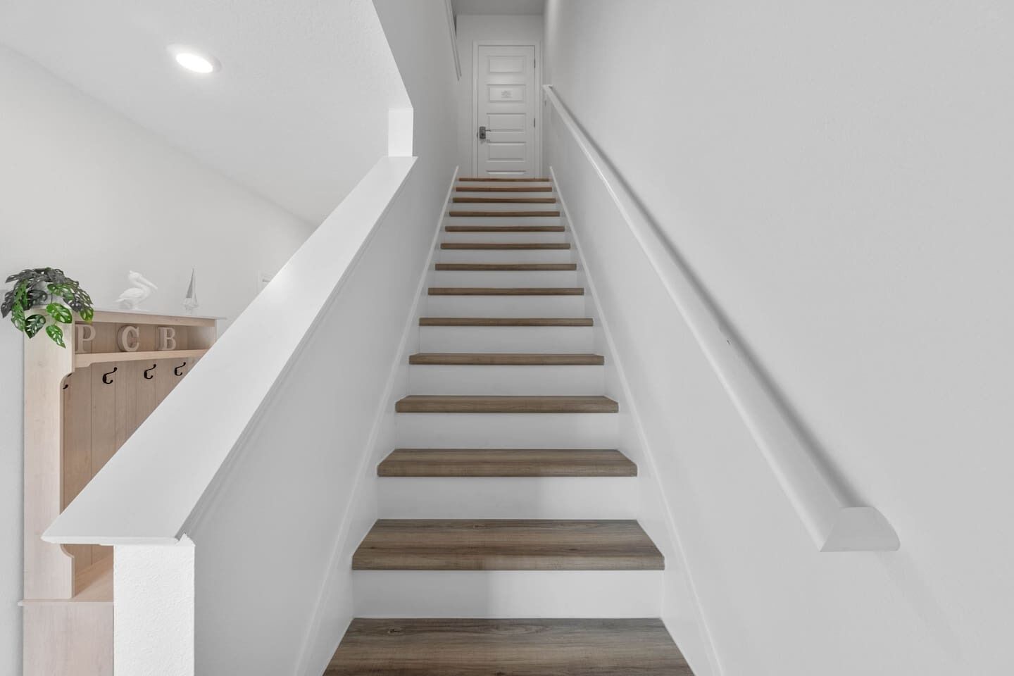 Una escalera de madera con paredes blancas que conduce a una puerta en la parte superior.