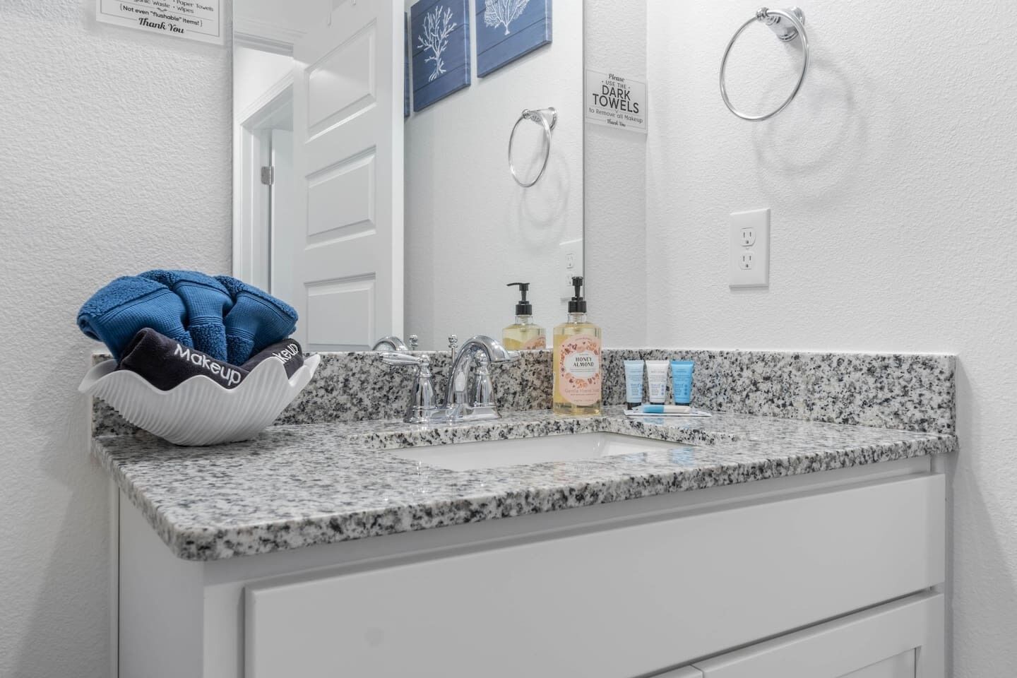 Un baño con encimera de granito, un lavabo, un espejo y un perchero para toallas.
