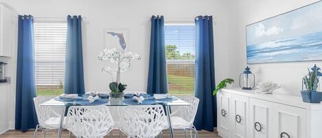 Un comedor con una mesa de vidrio, sillas blancas y un armario blanco con cajones.