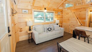 A cozy cabin interior with a sofa, two lamps, a dining table, and a window with a view of the outdoors.