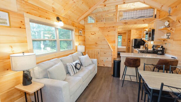 A cozy cabin interior with a wooden interior, a sofa, a dining table, and a kitchen area.