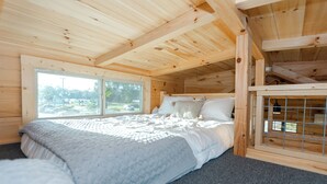 A wooden cabin bedroom with a bed, a window, and a view of the outdoors.