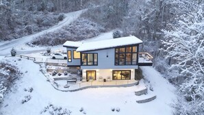 A modern two-story house with a large balcony, surrounded by snow-covered trees and a winding road. - Private Luxe Mountain View Getaway (Candler)