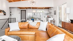 A modern living room with a leather sofa, a chandelier, and a view of the kitchen. - Private Luxe Mountain View Getaway (Candler)