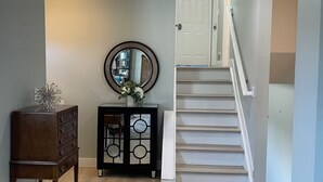Un pasillo con suelo de madera, un mueble de madera oscuro con espejo y una escalera blanca con barandilla.