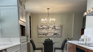 Una cocina moderna con suelo de madera clara, armarios blancos, una mesa de comedor con sillas y una araña.