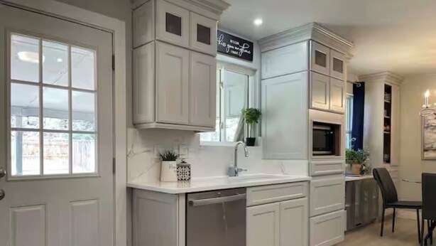 Una cocina moderna con armarios blancos, lavavajillas integrado y una zona de comedor con una silla negra.
