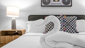 A neatly made bed with a white duvet, a wooden nightstand with a lamp, and patterned pillows. - Your Home in Fort Lauderdale: Modern 2BR Stay (Fort Lauderdale)