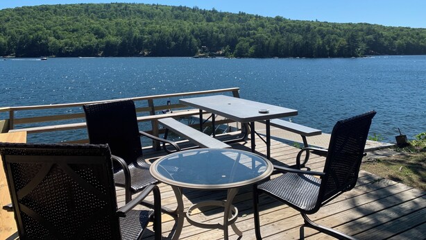 A wooden deck with a glass table and chairs overlooking a lake. - Gathering Home on Phillips Lake en route to Acadia-New Heat pumps (Dedham)