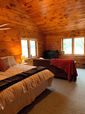 A wooden cabin room with a bed, a couch, a dresser, and two windows.