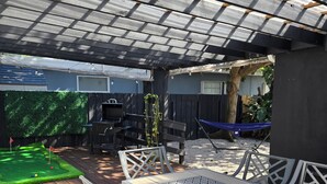 Un patio al aire libre con una mesa, sillas, una parrilla y una hamaca.