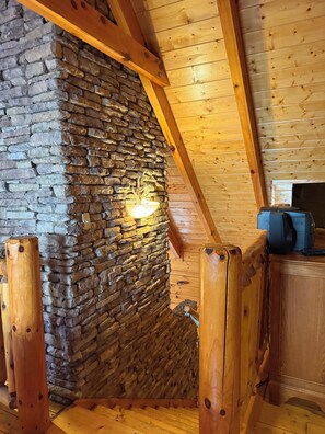 Ein gemütliches Blockhaus-Interieur mit einer Steinwand, Holzbalken und einem Schreibtisch mit Computer.