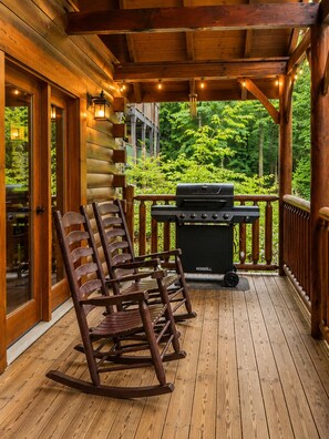 A wooden deck with a grill and rocking chairs. - Gatlinburg Log Cabin • Hot Tub • Fireplace • Game Loft • EV • Pet friendly (Gatlinburg)