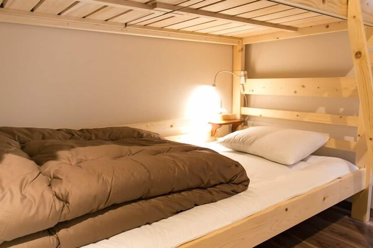 Un lit superposé avec une couette marron et des oreillers blancs, une lampe de chevet et une tête de lit en bois.
