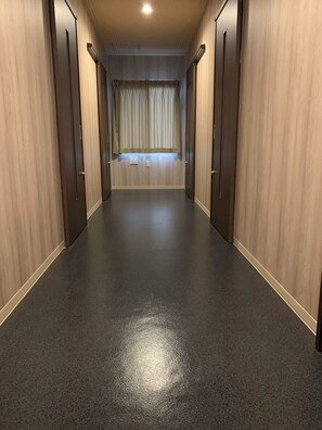 Un pasillo con paredes de madera y suelo oscuro, que lleva a una habitación con ventana y cortinas.