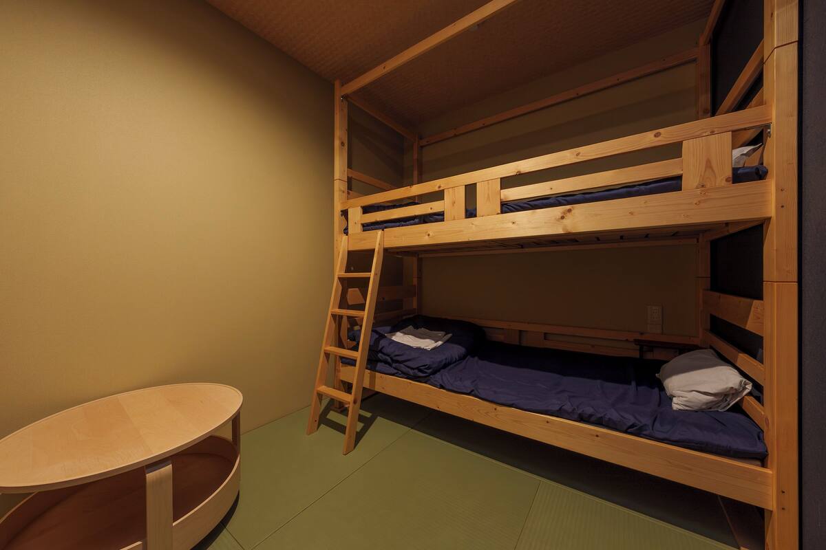 Une chambre avec un lit superposé, une échelle en bois, une petite table et un sol vert.