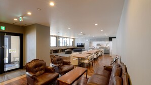 A spacious lounge area with leather sofas, wooden tables, and a kitchen in the background.