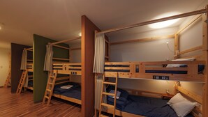 A dormitory room with bunk beds, wooden floors, and a ladder.