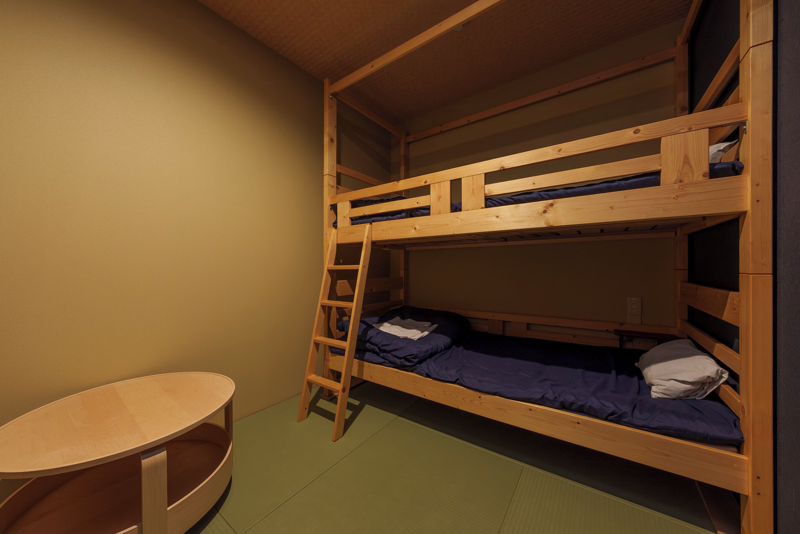 Une chambre avec un lit superposé, une échelle en bois, une petite table et un sol vert.