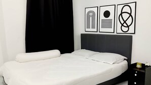 En pænt redt seng med hvide sengetøj, en sort sengegavl og et natbord med en lampe.