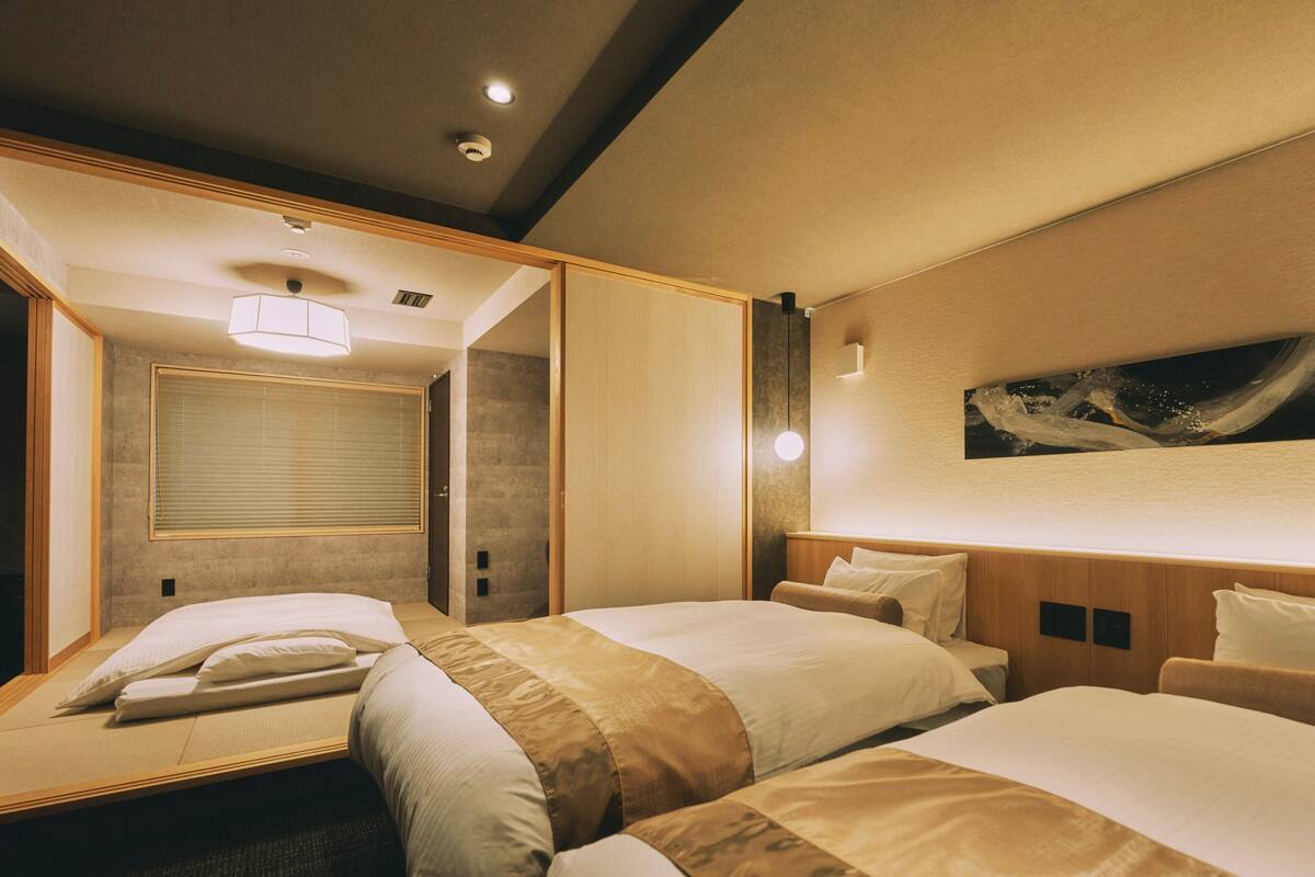 A hotel room with two beds, a large mirror, a painting on the wall, and a ceiling light.