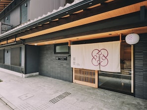 Hotellin sisäänkäynti, jossa on moderni julkisivu, kyltti, jossa on hotellin nimi, ja perinteinen japanilainen design-elementti.