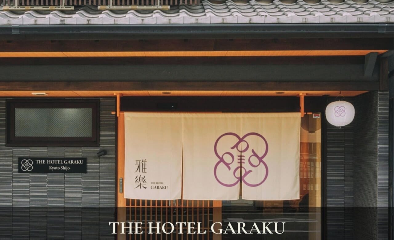 A hotel entrance with a traditional Japanese roof, a signboard with the hotel name, and a large banner with a logo.