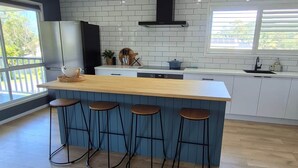 Une cuisine moderne dotée d’un îlot central, de tabourets de bar, d’un four encastré et d’une fenêtre offrant une vue sur l’extérieur.
