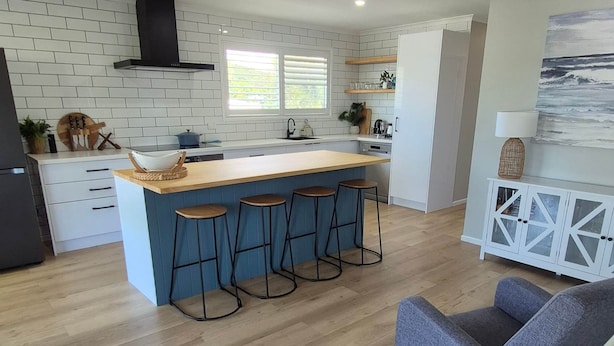 Une cuisine moderne dotée d’un îlot central, de tabourets de bar et d’un ventilateur de plafond.