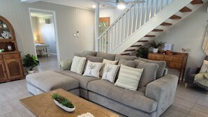 Un salon spacieux avec un canapé d’angle, une table basse en bois et un escalier menant à l’étage supérieur.