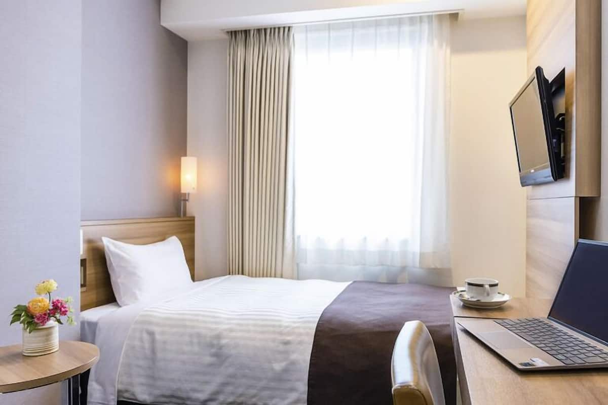 A hotel room with a bed, a laptop, a cup of coffee, and a TV on the wall.