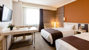 Habitación de hotel con dos camas, un escritorio con silla, televisor montado en la pared y ventana con cortinas.
