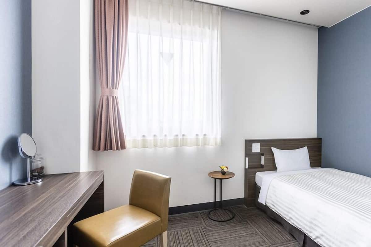 A hotel room with a bed, a chair, a small table, a mirror, and a window with curtains.