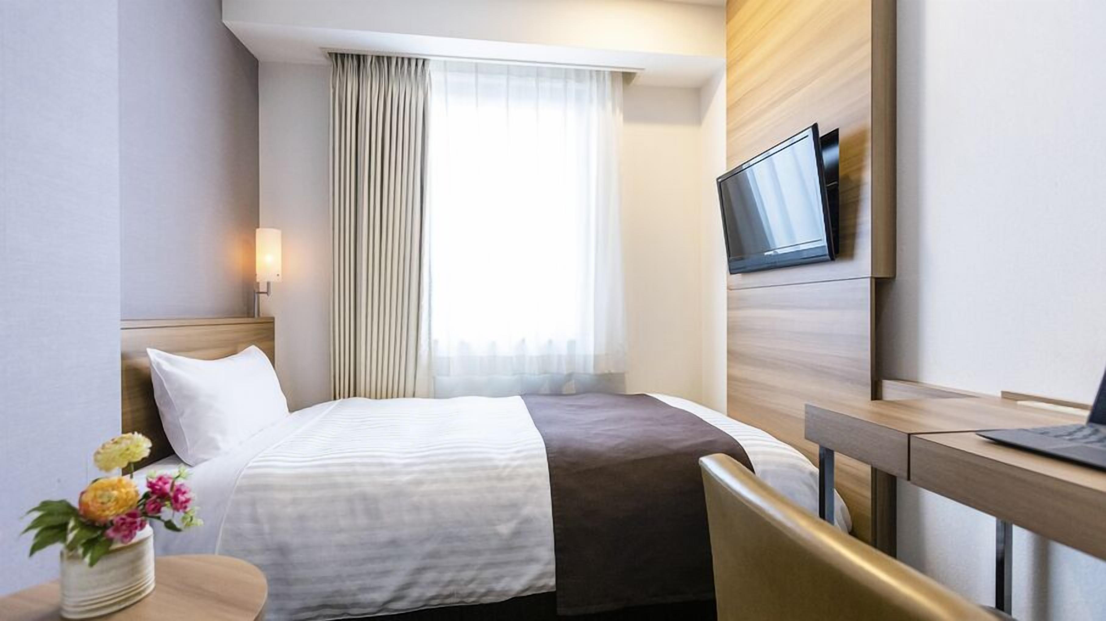 A hotel room with a bed, a desk, a TV, and a window with curtains.