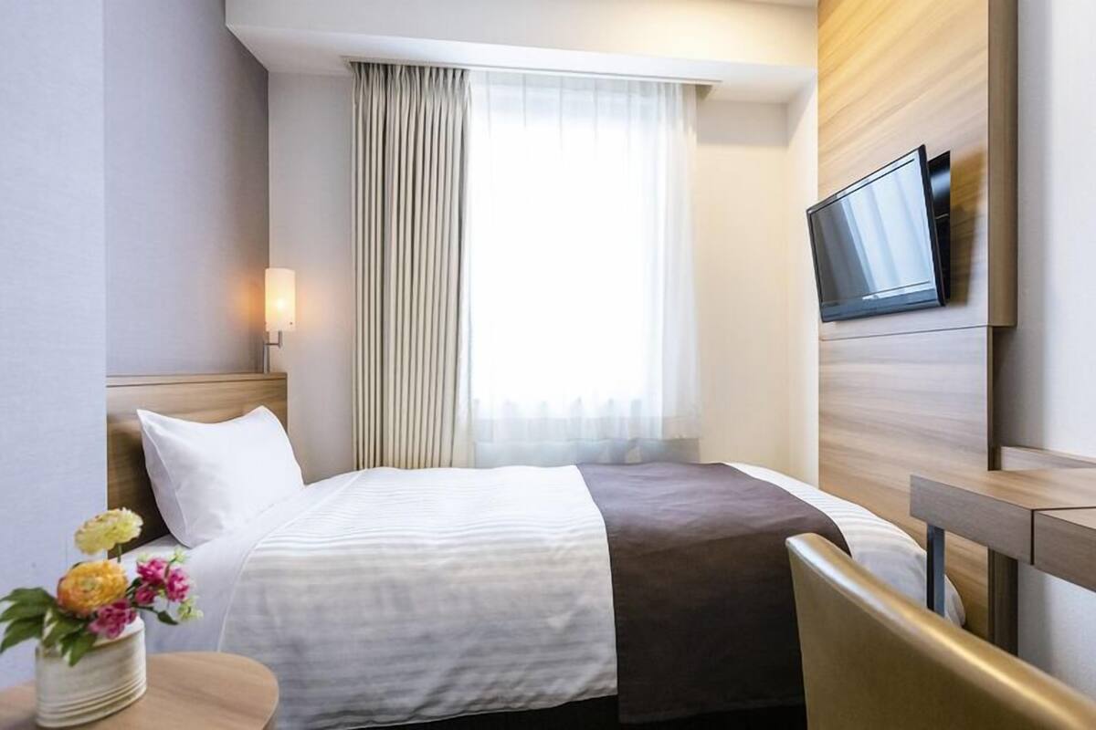 A hotel room with a bed, a desk, a TV, and a window with curtains.