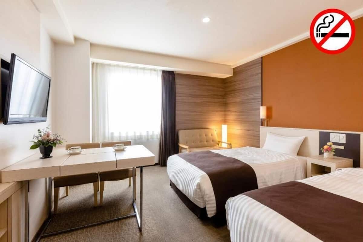 A hotel room with two beds, a desk, a TV, and a no-smoking sign.