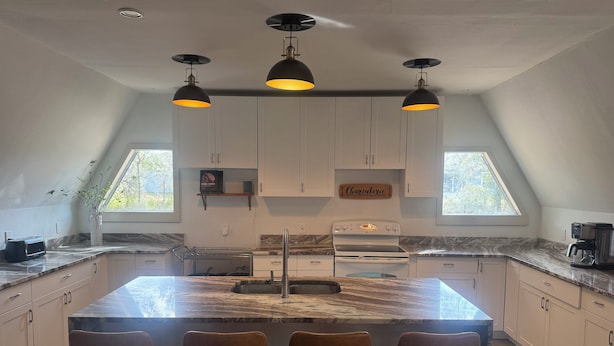 A modern kitchen with a large island, bar stools, pendant lighting, and a skylight. - Deland Dome Home- 98" TV - Open Kitchen (DeLand)