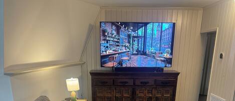Un salón con un televisor de pantalla plana grande, una mesa de centro de madera y un sofá modular gris.