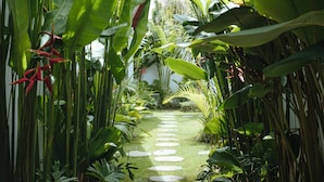 Un sentier de jardin, bordé de pierres plates, serpente au milieu d’une végétation tropicale luxuriante.